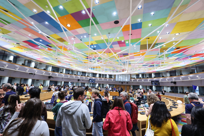 Une foule de visiteurs dans une salle de réunion du Conseil au plafond coloré.