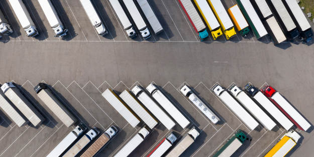 An aerial view of numerous articulated lorries parked in diagonal rows in a large lorry park.